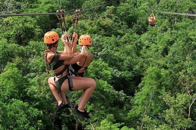 Visitor riding a zip-line high above the jungle at Xplor